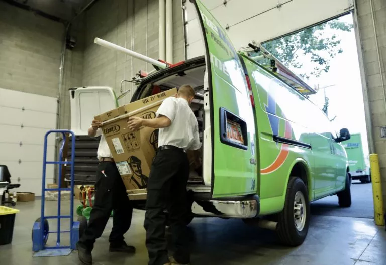 technicians loading an air conditioning unit into the back of a service van
