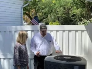 HVAC technician talking to homeowner about outdoor AC unit while looking at it